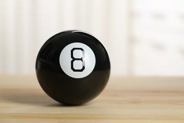 Magic eight ball with on wooden table, closeup. Space for text