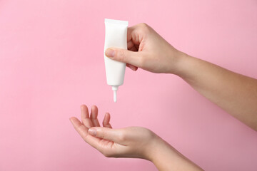 Woman applying cosmetic cream from tube onto her hand on pink background, closeup