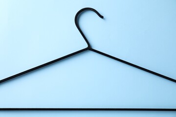 One black hanger on light blue background, top view