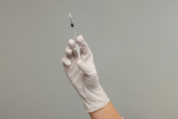 Doctor holding medical syringe on grey background, closeup