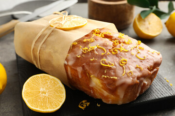 Wrapped tasty lemon cake with glaze and citrus fruits on grey table, closeup - obrazy, fototapety, plakaty