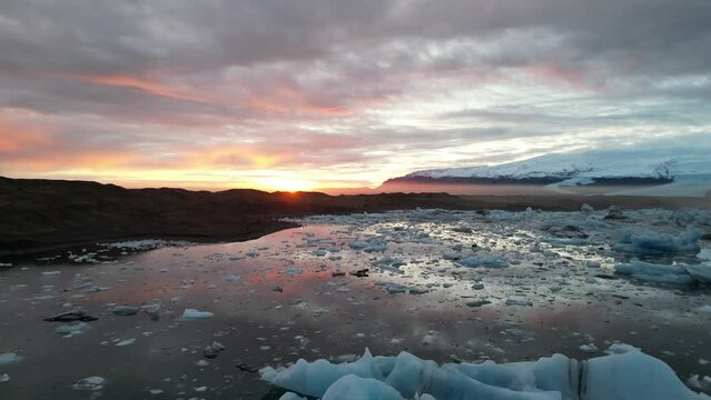 Spectacular drone aerial view of a beautiful sunset reflecting off Iceland's largest glacier, Glacial Lake, floating giant pieces of glacier, and land with cars running on it Jokulsarlon and Vatnaj&ouml;ku