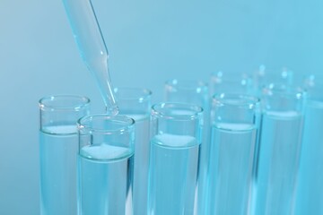Laboratory analysis. Dripping reagent into test tube on light blue background, closeup