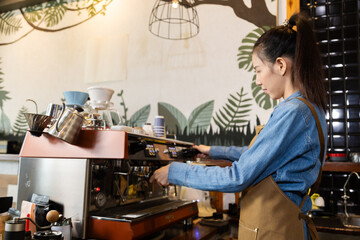 Asian barista female making hot coffee from professional machine standing behind cafe shop counter bar, young waitress worker or small business entrepreneur wearing apron working in eatery cafeteria