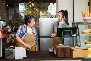 Young Asian barista female smiling happy with first online order from modern technology smartphone,...