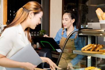 Asian young small business owner female service customer ordering using POS cash machine in cafe coffee shop restaurant, barista waitress worker standing in counter bar working in cozy workplace
