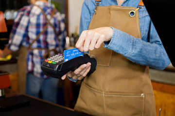 Closeup waitress hand holding credit card swipe on wireless digital payment machine, worker wearing apron working in cafe retail small business using modern cashless touchless payment transaction
