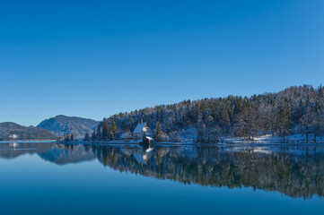 Winterlandscape at a lake with mirroring, reflections and blue sky