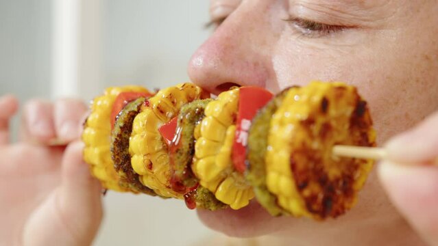 Vegan woman biting and eating vegetarian barbecue vegetables on skewer. Organic clean food, healthy balanced diet eating.
