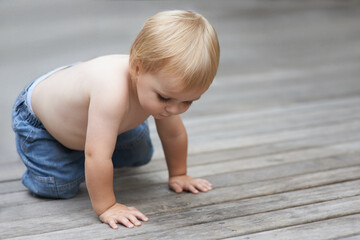 Naklejka premium Toddler, playing on floor outdoor for development with relax, curiosity and early childhood in backyard of home. Baby, child and crawling on ground for wellness, milestone or exploring with innocence