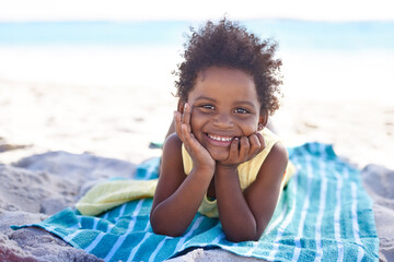 Smile, african child and portrait on beach sand, towel and summer holiday with sunshine in nature. Black girl, young and happy face to relax on vacation, cape town and ocean for wellness in outdoor