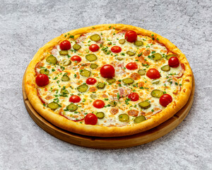 Homemade Italian style pizza with cheese, cucumbers, green onions, cherry tomatoes and spices close-up on a wooden board on the table. Horizontal