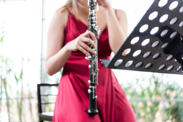 Beautiful young woman in a red dress playing the clarinet .,Classical musician oboe playing..
