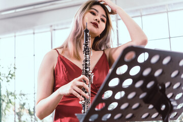 Beautiful young woman in a red dress playing the clarinet .,Classical musician oboe playing..