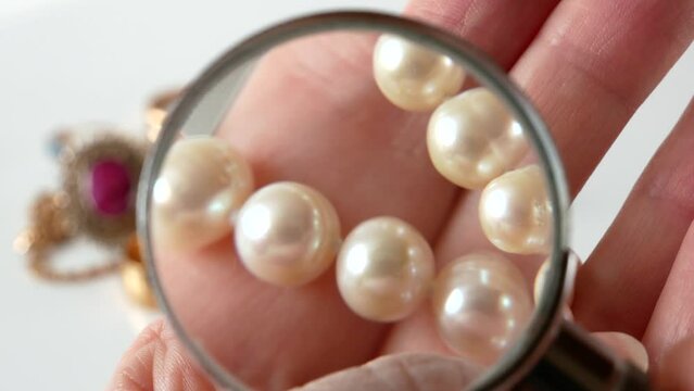 white pearls necklace and magnifying glass in jeweller's hand, pawnshop concept