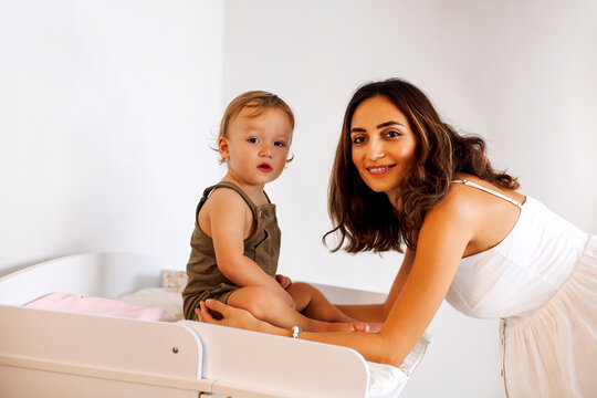 Portrait of family young mother standing near changing table with cute little baby boy on it