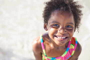 Wet, happy child and portrait on beach sand, swimsuit and summer holiday with sunshine in nature. Black, young girl and smile face for swim on vacation, cape town and ocean for wellness in outdoor
