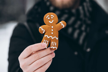 Close-up, gingerbread in a man's hand against a blurred background outside. A delicious gingerbread man decorated with icing. Traditional Christmas dessert. Copy space.