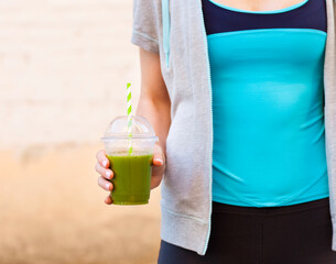Woman drinking vegetable smoothie after fitness running workout on summer day