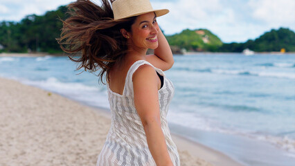 Young attractive woman smiling and walking on the beach at sunrise on her tropical vacation, happy white woman enjoying the beach
