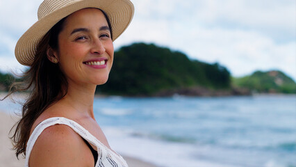 Happy young white woman wearing hat feeling the sea breeze. Beautiful smiling girl relaxing and enjoy the sun at seaside. 
 - obrazy, fototapety, plakaty