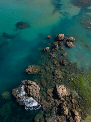 Waves against rock formation in turquoise sea in Malta aerial top down. Vertical background photo. Natural sea colors palette in Mediterranean paradise.