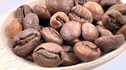 Top view of a pile of scattered aromatic roasted brown coffee beans with a wooden scoop. Coffee beans in a wooden spoon. Fragrant coffee, coffee drinks.