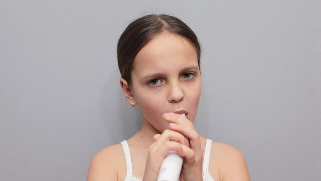 Dental health joy. Electric brush excitement. Pretty funny brown haired little girl brushing her teeth with electric toothbrush isolated on gray background