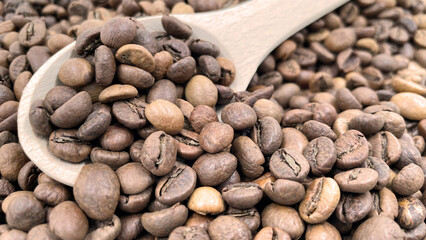Food background texture of roasted coffee beans with a full shovel. A pile of scattered aromatic roasted brown coffee beans with a wooden scoop. Coffee beans in a wooden spoon.