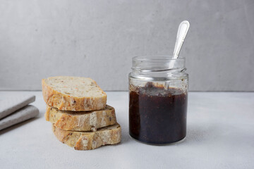 Strawberry jam in a glass jar on a light gray background with sliced ​​bread. Composition with delicious homemade jam. Breakfast and snack concept.