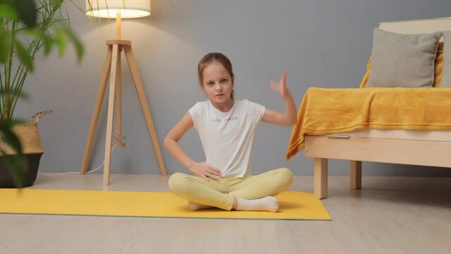 Leisure activities for children. Yoga positions for kids. Caucasian little girl with brown hair and ponytail doing sports exercises warming up her body on mat at home