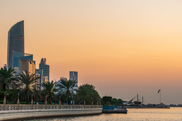 Abu Dhabi skyline at sunset, from the corniche, in the UAE, hazy dusk colored sky, pink and orange,...