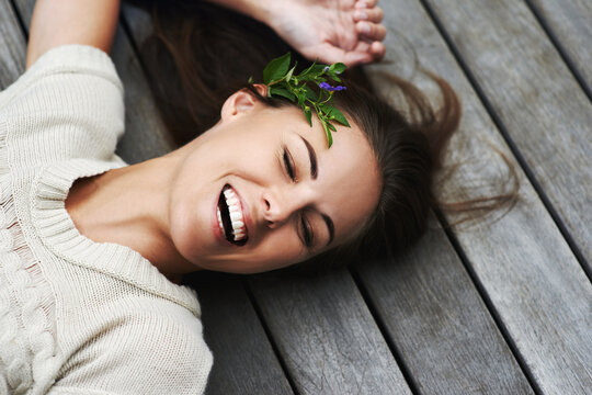 Woman, face and happy on porch for relax outdoor in backyard with flower, lying down and rest in home. Person, spring and smile on wooden deck in garden of house or apartment with carefree or casual