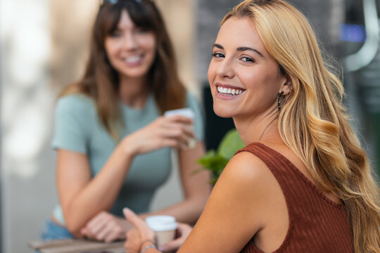 Two attractive friends enjoying coffee together while talking and laughing sitting on the terrace of a bar.