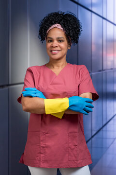 Freundliche weibliche Reinigungskraft in Arbeitskleidung und Gummihandschuhen mit verschr&auml;nkten Armen