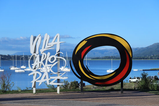Poster of 3d letters with the name of the city Villa Carlos Paz. Corporeal sign of the tourist city of Córdoba Argentina. Sign with a background of Lake San Roque, boats, cars and people.