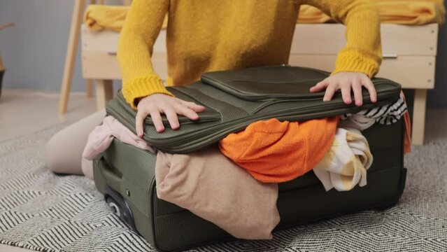 Unrecognizable faceless woman packing suitcase pack her clothes getting ready for vacation at home going on tourist trip cannot zip bag full of attires