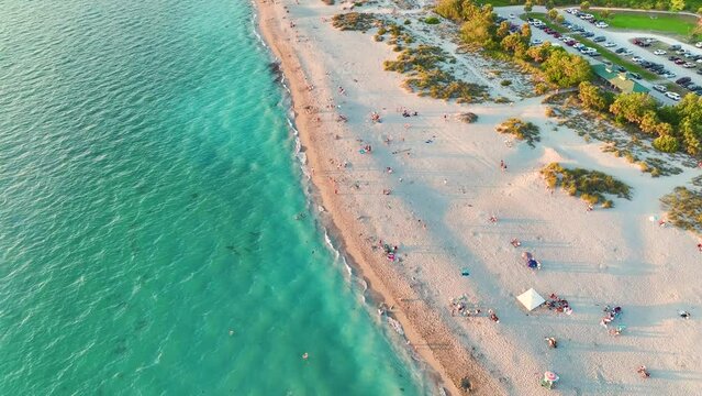 View from above of evening Blind Pass beach with white sands and relaxing tourists on Manasota Key, USA. People enjoying vacation time swimming in Mexica gulf water and resting on warm Florida sun