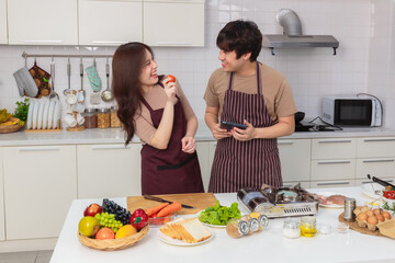 Loving young Asian couple prepare ingredient for cooking together by using instruction from tablet in home kitchen