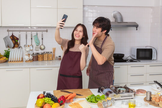 Lovely young Asian couple take a selfie photo while prepare ingredient for cooking together in home kitchen