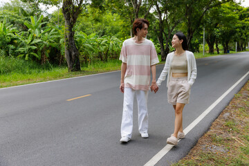 Obraz premium Young Asian couple hold their hands looking at each others and walking on the road while travel with happiness