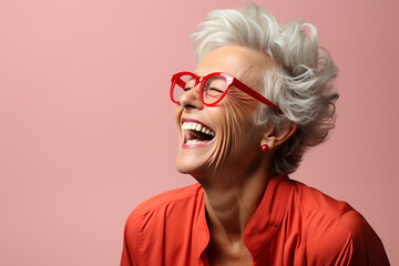 beautiful elderly woman 60 years old in profile on a pink background laughing loudly with teeth, gray hair, glasses with bright frames