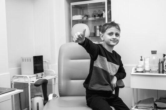 black and white classic photo, a little boy, a fair-haired teenager, sits in the otolaryngologist's office, waiting for an examination, emotional, but smiling and showing everything ok. 