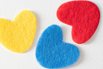 Three felt hearts on white background.  Yellow, red, and blue felt hearts.