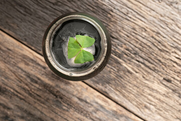 Dark, Irish beer with shamrock leaf.  Looking down at a stout beer topped with a fresh, green shamrock leaf, on a weathered wooden background. - Powered by Adobe