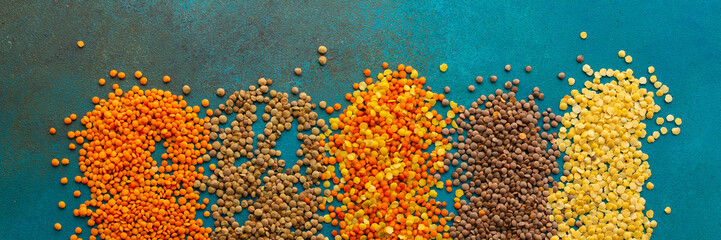 Multi-colored lentils on an emerald green background, scattered yellow and brown, green and orange lentils, healthy legumes banner, top view