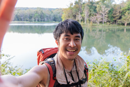 Happy Asian traveller man takes a selfie photo on a lake at the mountain.