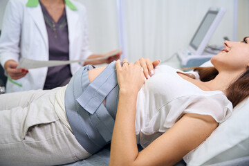 Blurred partial gynecologist checking electrocardiogram of pregnant woman belly