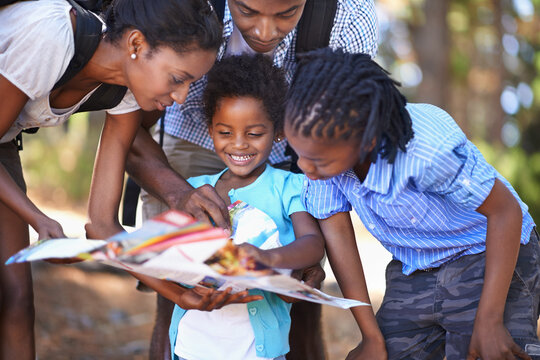 Travel, map and children with parents in a forest for location, direction or search outdoor together. Paper, navigation or black family reading hiking guide for woods trekking, adventure or discovery