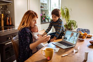 Mother with baby and son during telehealth appointment with doctor on laptop at home